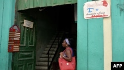 Una mujer parada junto a dos señales de negocios privados en Cuba.