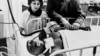 La esposa de Benny "Kid" Paret y su manager, Manuel Alfaro, junto al boxeador, inconsciente en una cama del hospital Roosevelt, tras la pelea con Emile Griffith, en marzo de 1963. (Foto AFP/Archivo)
