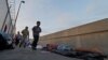 Varias personas que se dirigen a cruzar la frontera pasa delante de varios solicitantes de asilo de Guatemala y Cuba que esperan en un puente a poder entrar en EEUU. (Archivo)