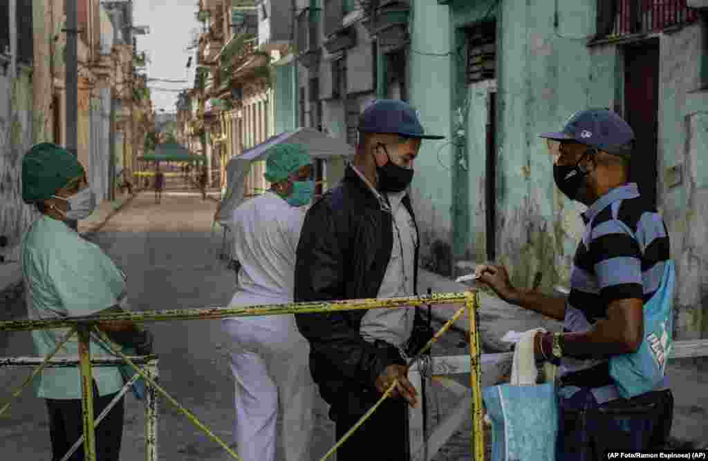 Un residente muestra su identificación a un oficial de policía que está limitando el acceso a un vecindario como una forma de frenar la propagación de la pandemia de COVID-19,  22 de febrero de 2021. (AP Foto/Ramon Espinosa)